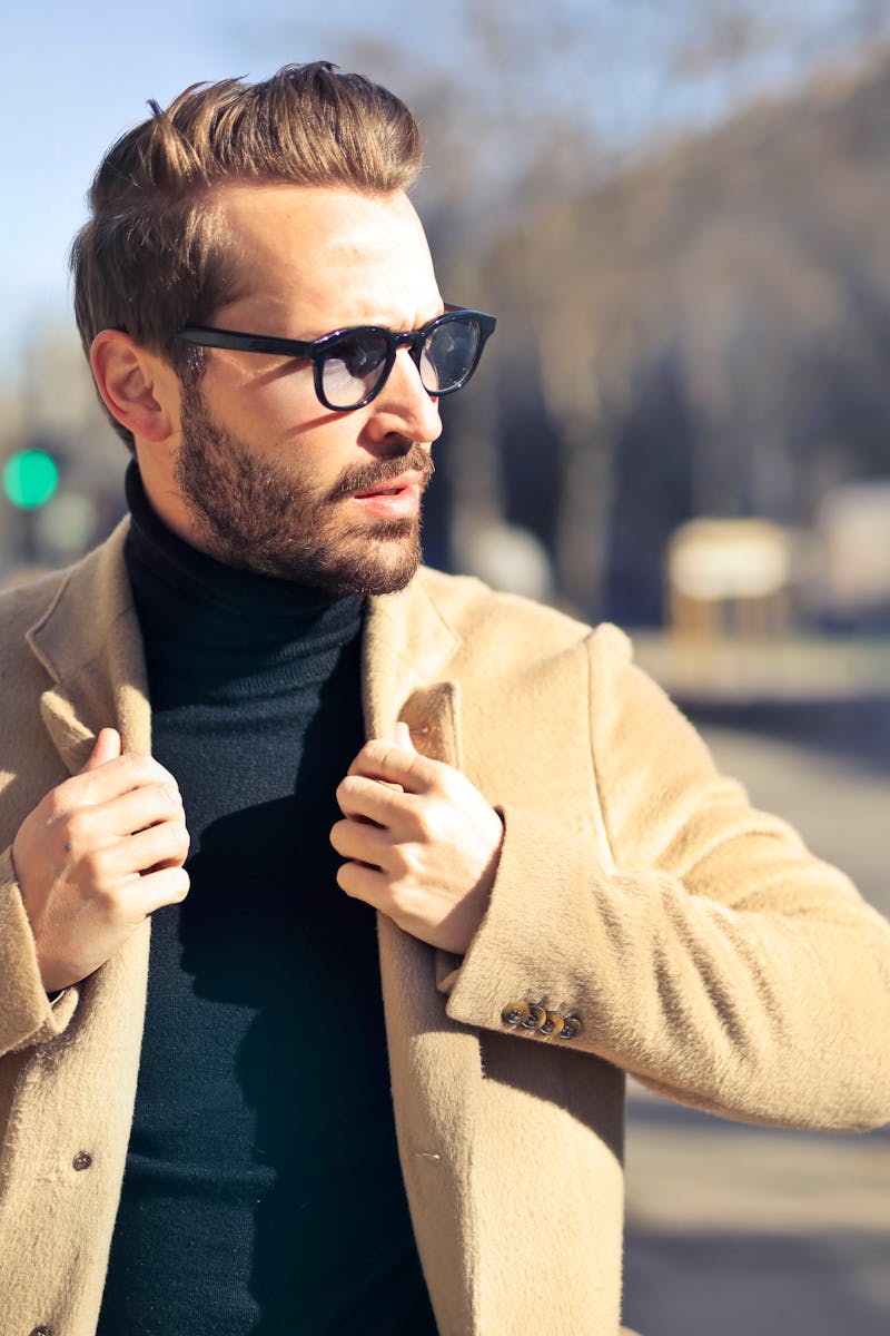 Fashionable young man with sunglasses poses outdoors in a sunny Budapest street scene.